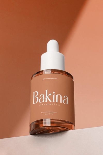 A clean, studio-lit photograph of a serum bottle placed on a geometric pedestal against a warm-toned, monochromatic background.